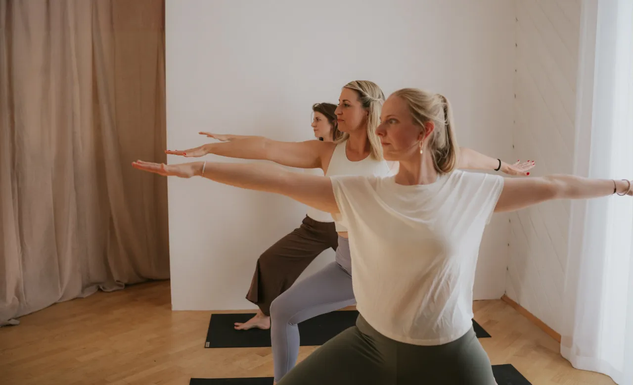 Drei Frauen in der Kriegerposition im hellen Yogaraum der Soul Oase
